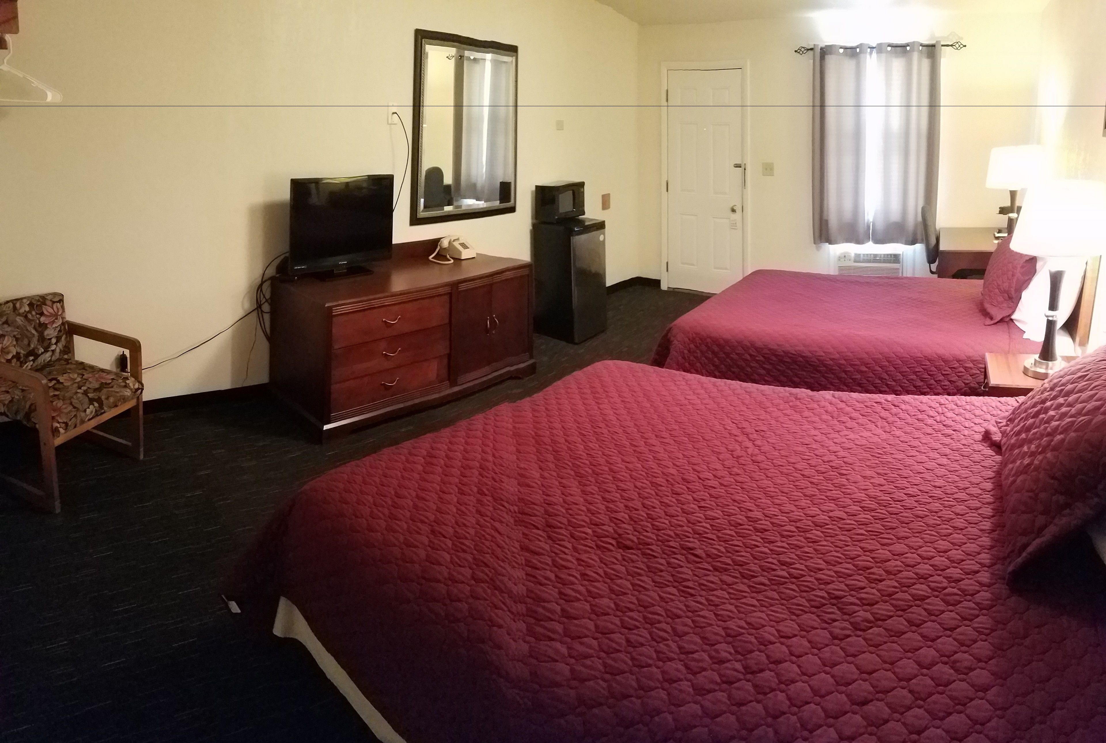 Una habitación de hotel con dos camas, televisión, refrigerador, escritorio con lámpara y una silla.