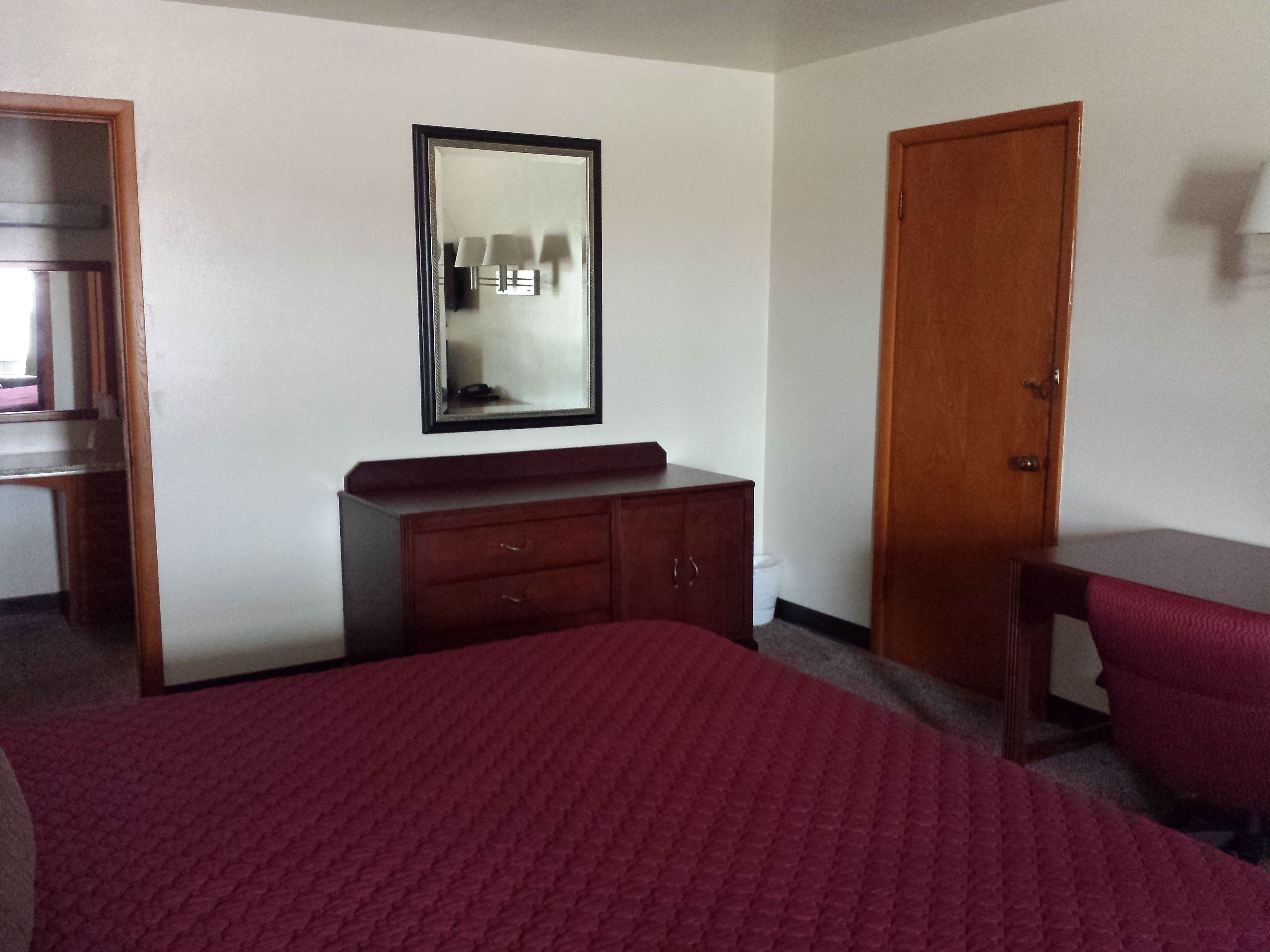 A hotel room with a bed, a wooden dresser, a mirror, and a door.