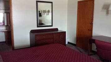 A hotel room with a bed, a wooden dresser, a mirror, and a door.