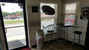 A room with a wooden floor, a red patterned mat, a trash bin, and a window with blinds.