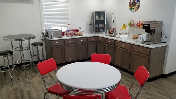 A compact kitchen with a round dining table, red chairs, and a coffee machine.