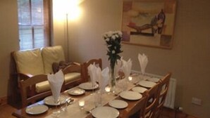Una mesa de comedor dispuesta con platos, servilletas y un jarrón de flores, rodeada de sillas de madera.