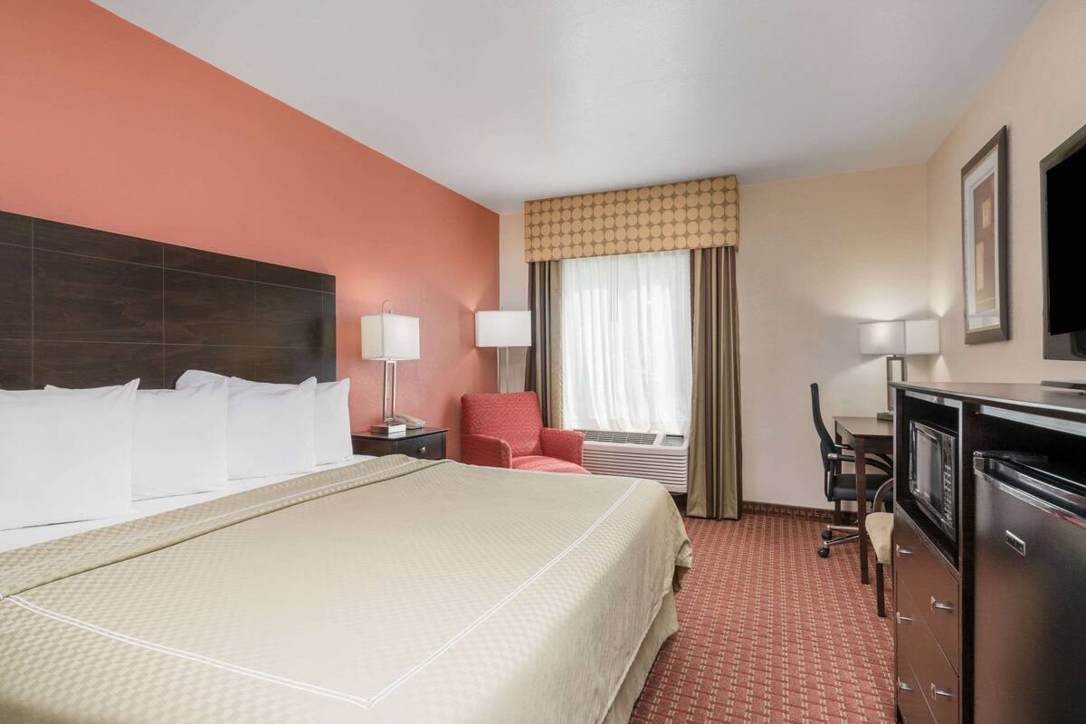 Een hotelkamer met een groot bed, een bureau, een stoel, een televisie en een raam met gordijnen.