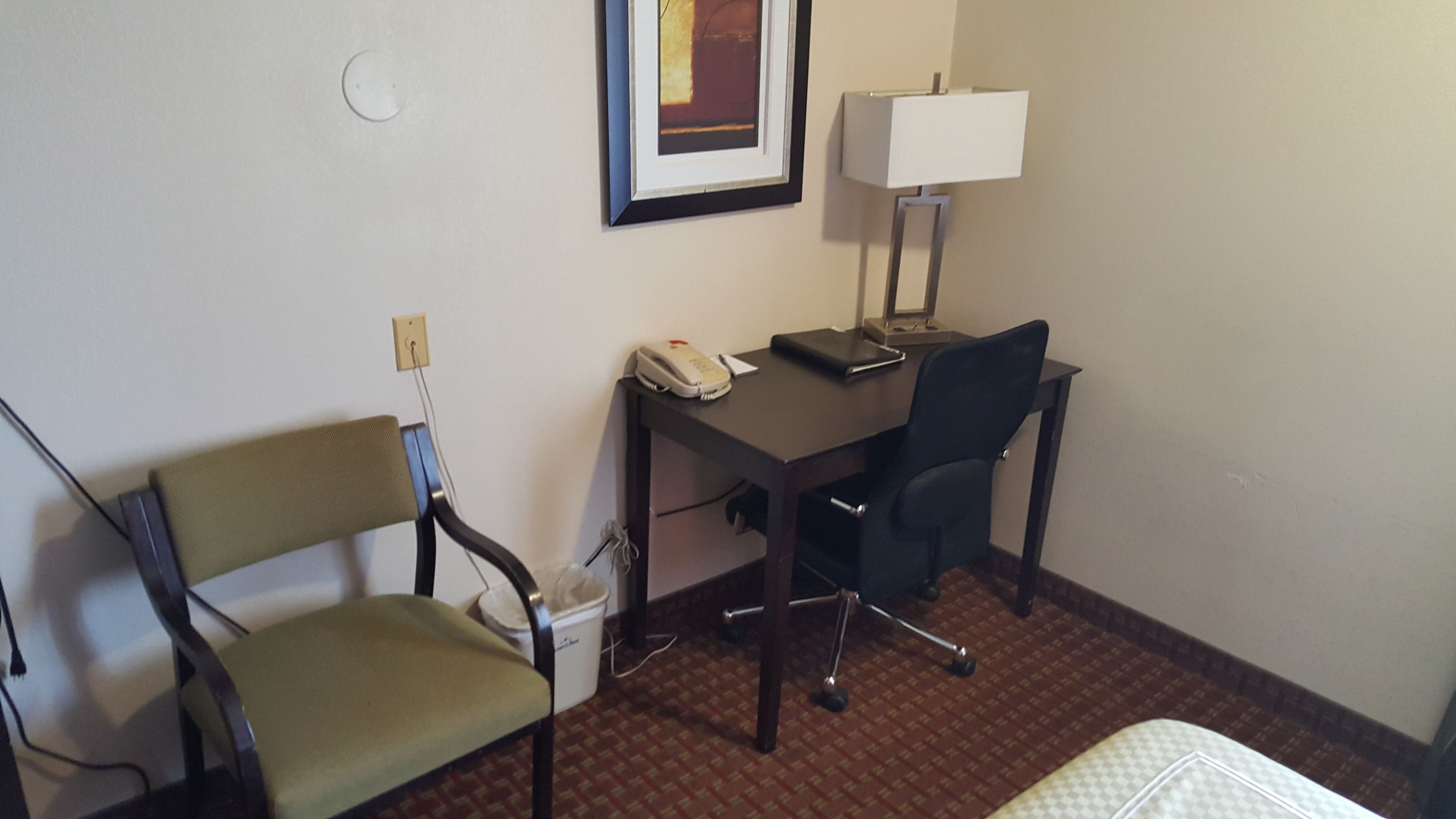 Una habitación de hotel con escritorio, dos sillas, una lámpara y una cama.