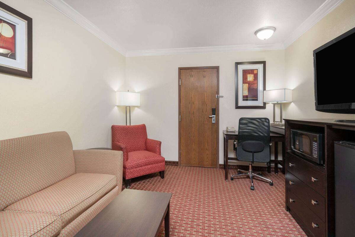 Een hotelkamer met een bank, fauteuil, bureau, stoel, televisie en een dressoir.
