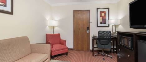 A hotel room with a sofa, armchair, desk, chair, television, and a dresser.