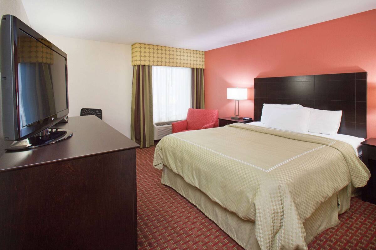 Hotelkamer met een bed, een bureau met televisie, een stoel, een nachtkastje met lamp en een raam met gordijnen.