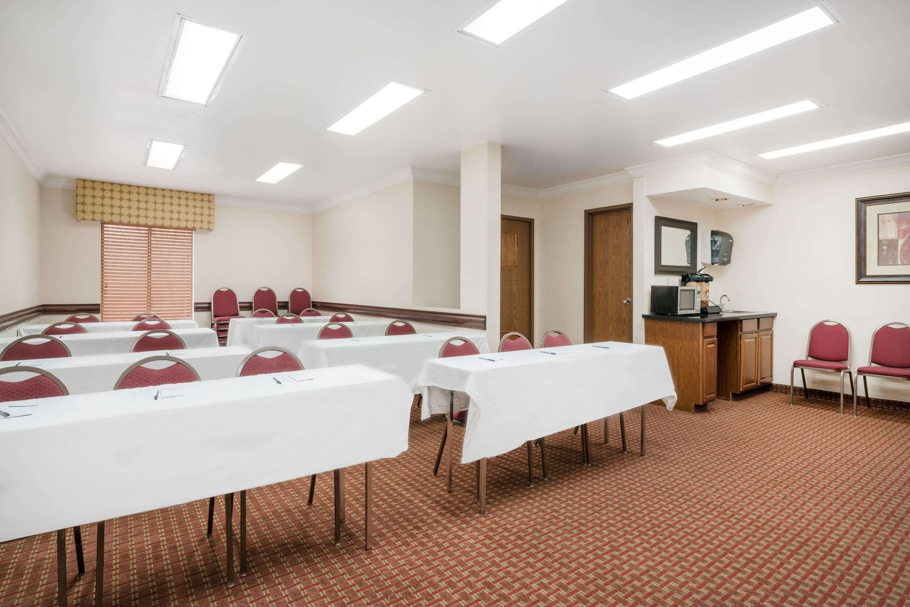 A conference room with white tables, red chairs, a wooden cabinet, and a patterned carpet.