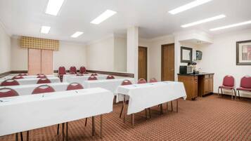 A conference room with white tables, red chairs, a wooden cabinet, and a patterned carpet.