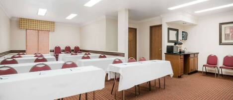 A conference room with white tables, red chairs, a wooden cabinet, and a patterned carpet.