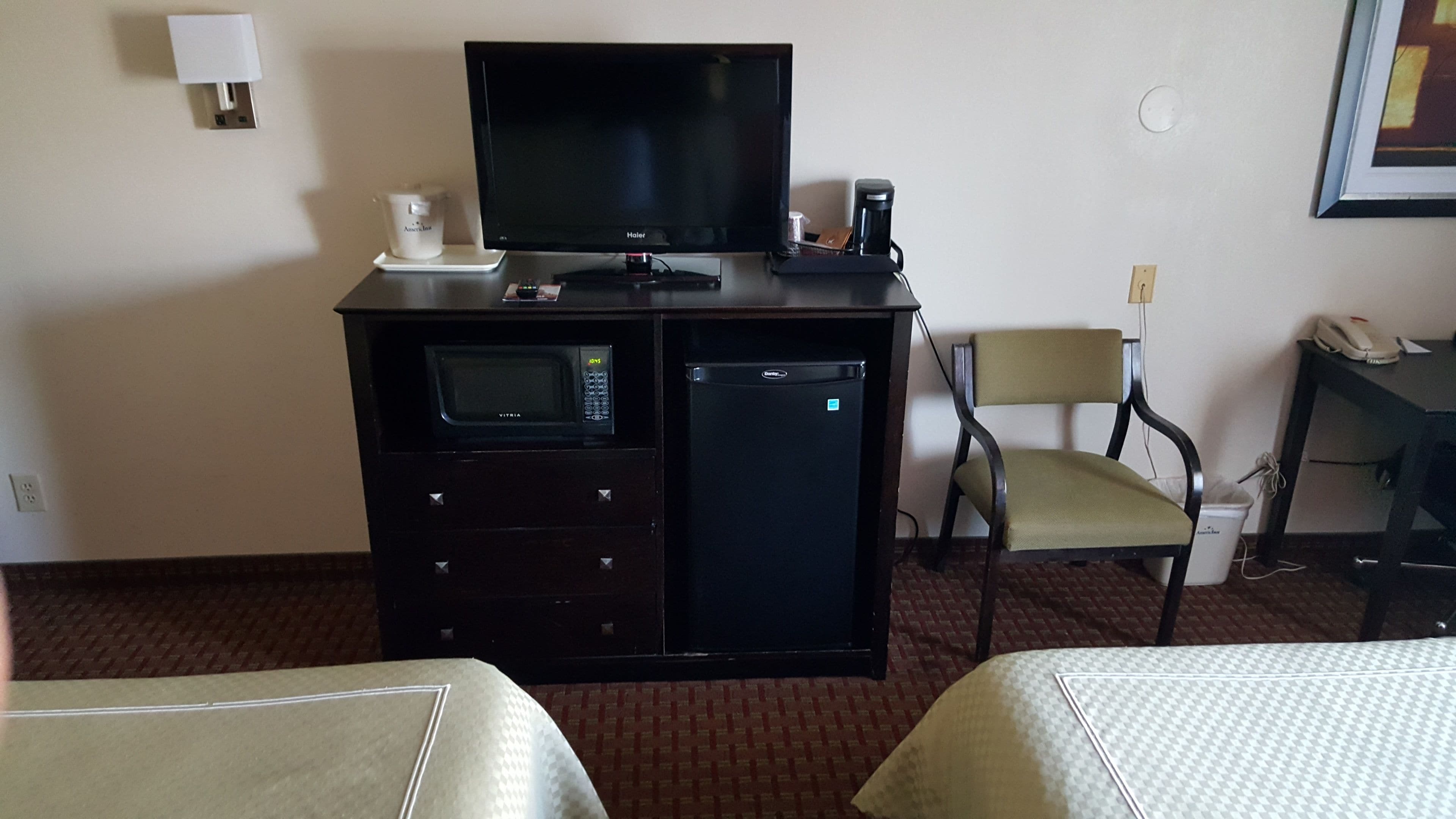 Una camera d'albergo con TV, minibar, forno a microonde e un piccolo frigorifero. Sono presenti due letti e una sedia.