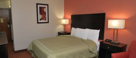 A hotel room with a bed, two bedside tables with lamps, a chair, and a door.