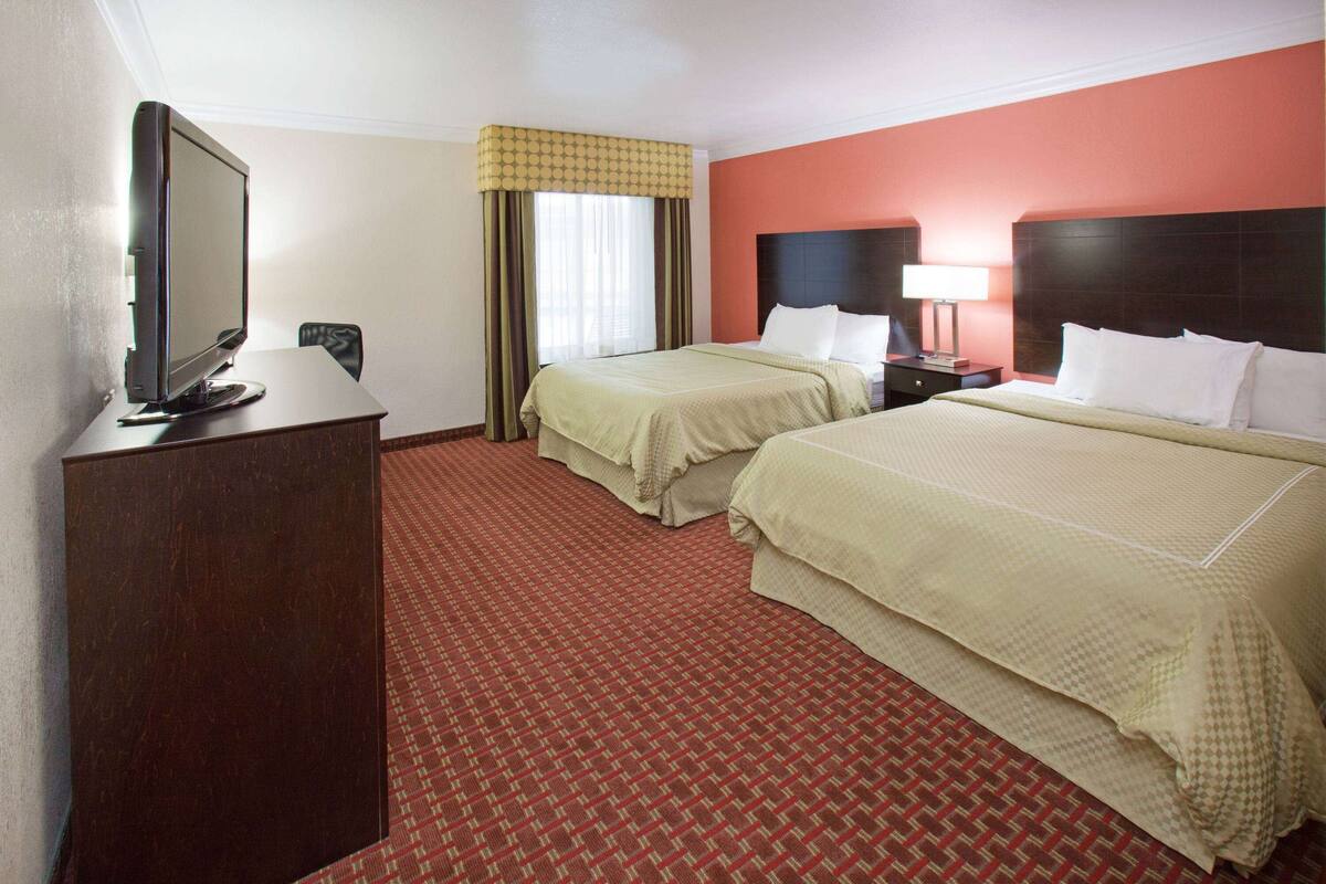 Een hotelkamer met twee bedden, een televisie, een bureau en een raam met gordijnen.