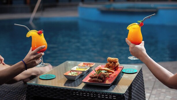 Ein Esstisch am Pool mit Getränken, frittierten Speisen und kleinen Schalen.