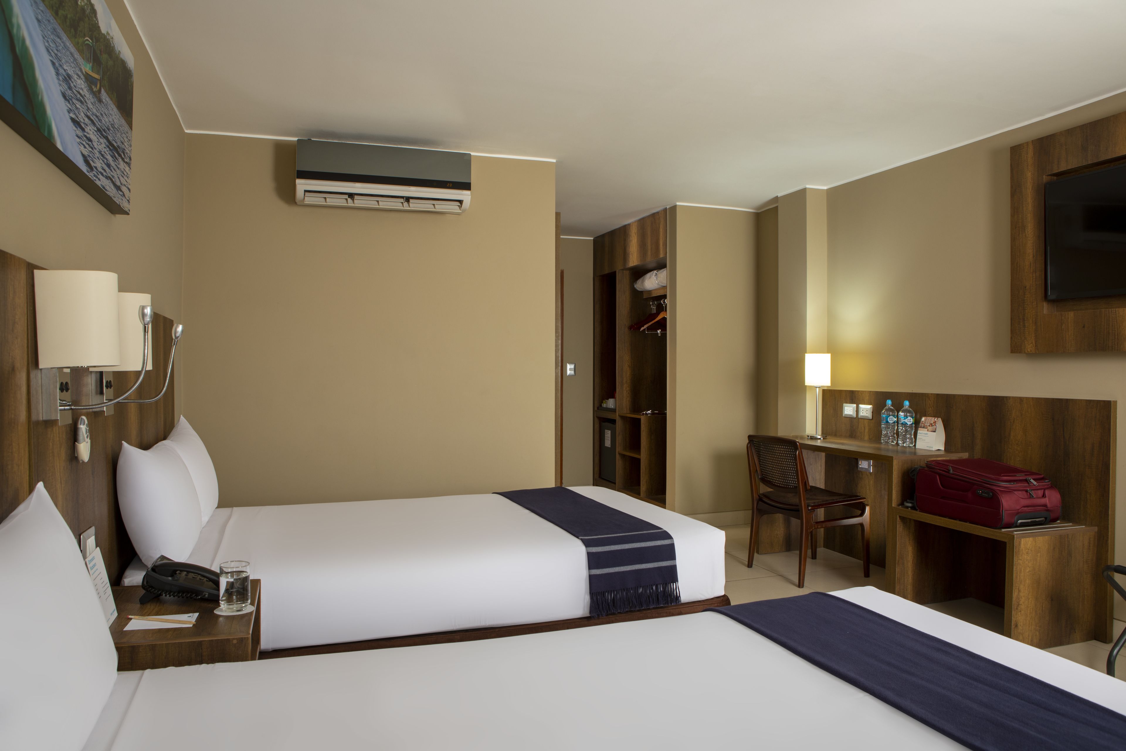 Habitació d'hotel amb dos llits, una taula de treball, una cadira, un armari i una televisió.