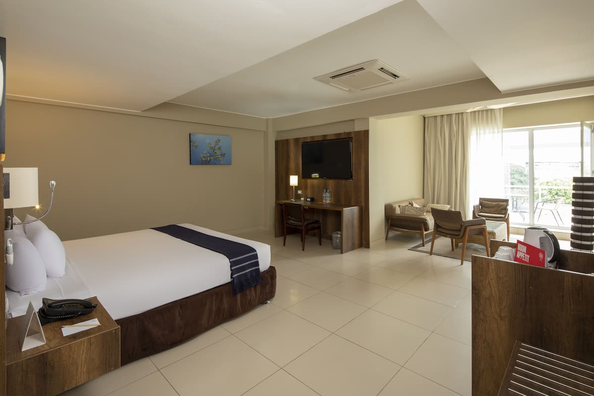 A hotel room with a bed, desk, chairs, and a TV.