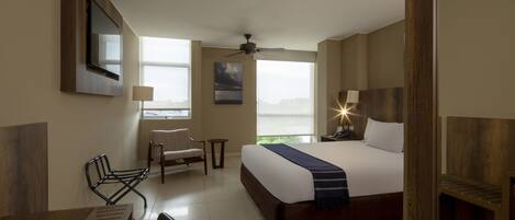 A hotel room with a bed, a desk, a chair, a TV mounted on the wall, and a window with a view.