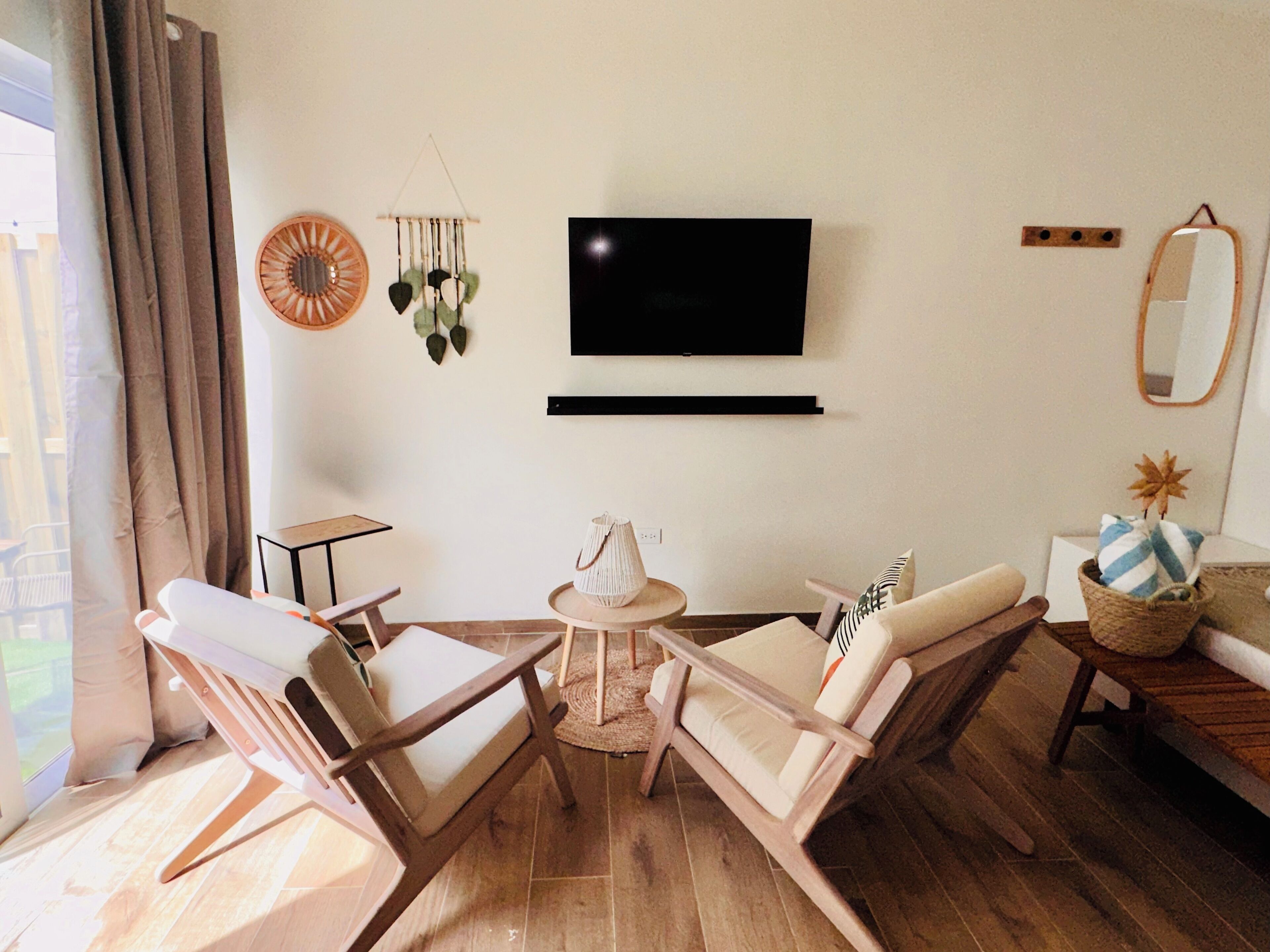 A living room with two wooden chairs, a small round table, a television mounted on the wall, and a mirror.