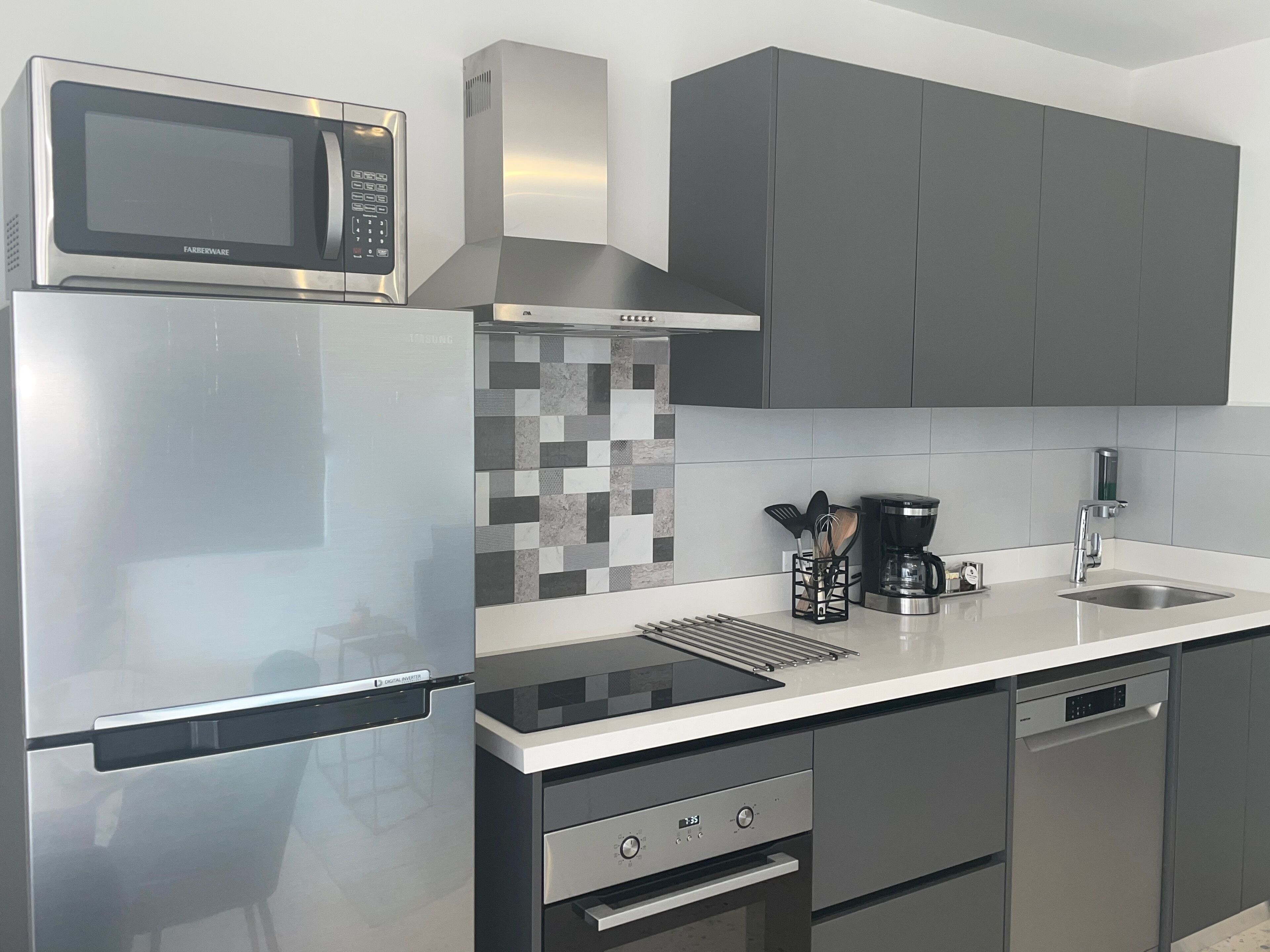 Una cocina moderna con un refrigerador de acero inoxidable, un microondas, una cafetera y un lavavajillas.