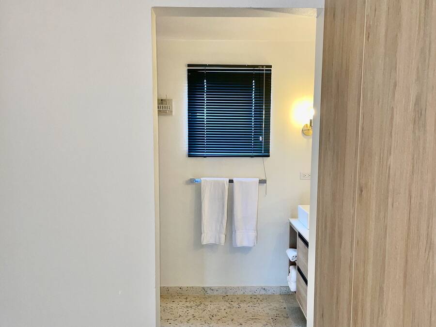 A narrow hallway leading to a bathroom with a window, a towel rack, and a sink.