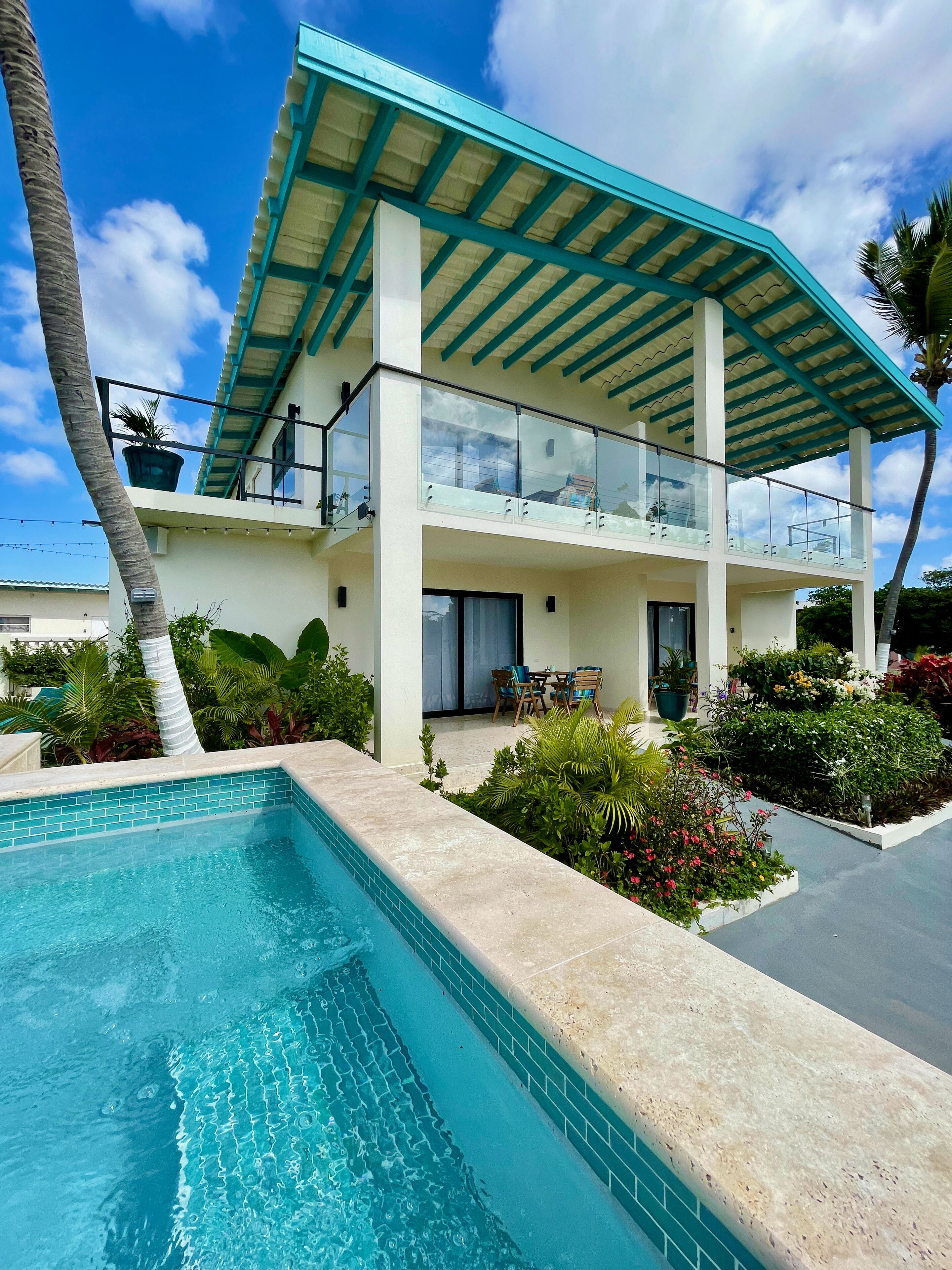 Una casa de dos pisos con piscina, un patio cubierto y jardines exuberantes.