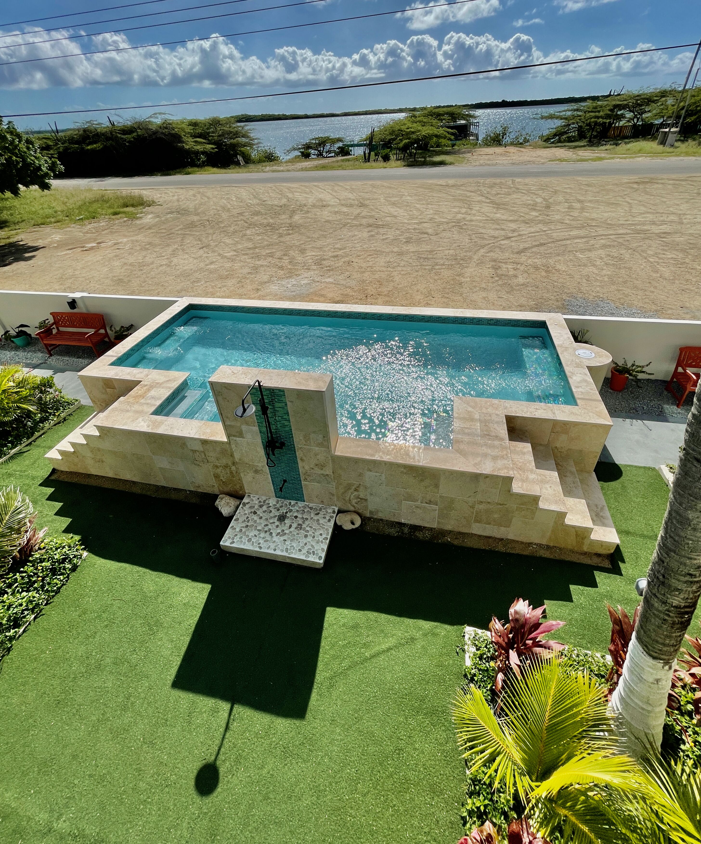 A rectangular pool with a stone border, surrounded by artificial grass and potted plants.