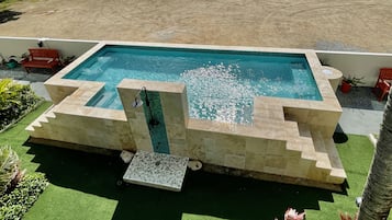 A rectangular pool with a stone border, surrounded by artificial grass and potted plants.