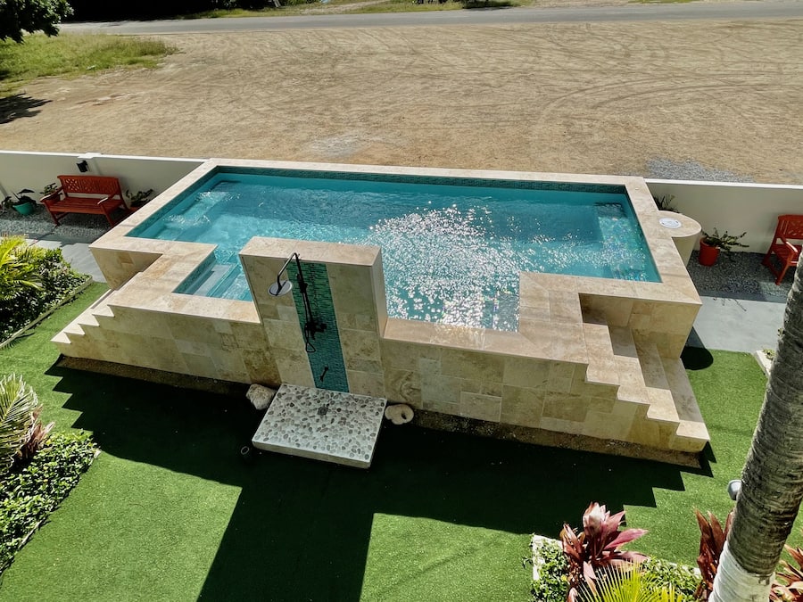 A rectangular pool with a stone border, surrounded by artificial grass and potted plants.