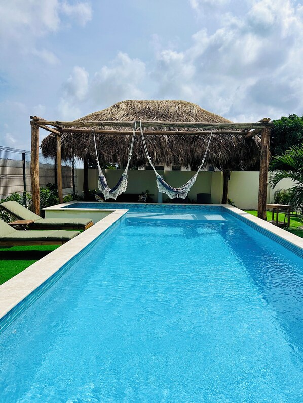 A swimming pool with a thatched roof structure and hammocks. - Vistalmar Ocean Suites (Oranjestad)