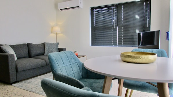 A living room with a grey sofa, a blue armchair, a small table with a bowl, a lamp, and a TV. - Vistalmar Ocean Suites (Oranjestad)