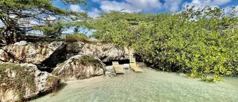 Une zone de plage avec une eau claire, des formations rocheuses et un espace aménagé avec des chaises longues.
