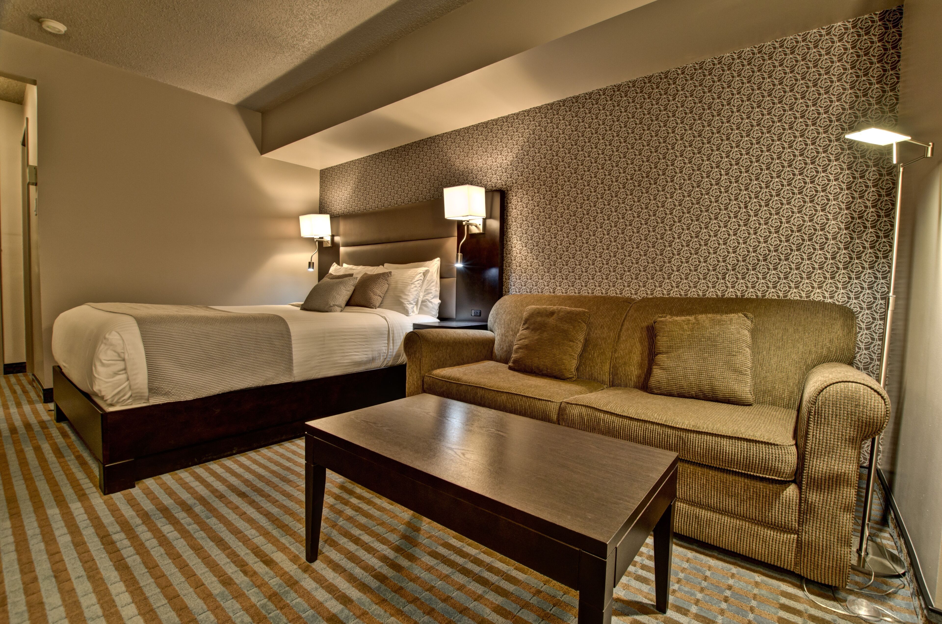 Habitación de hotel con cama, sofá, una mesa de centro y papel tapiz estampado.