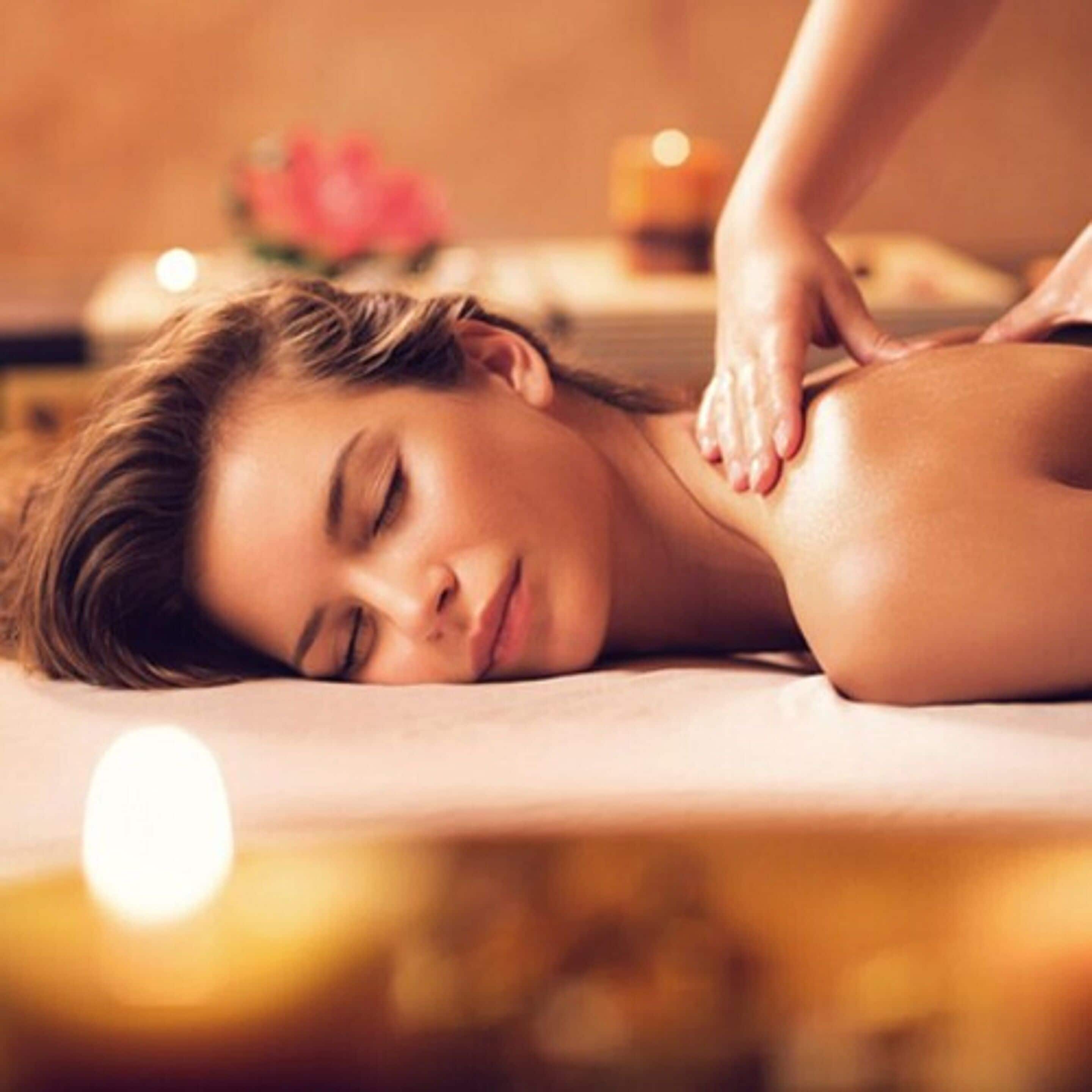Une personne reçoit un massage du dos dans un spa, avec des bougies et des fleurs en arrière-plan.
