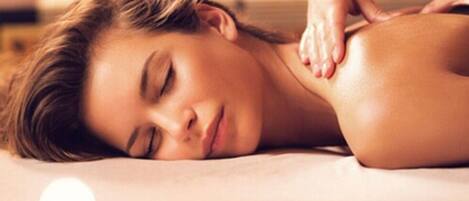 Une personne reçoit un massage du dos dans un spa, avec des bougies et des fleurs en arrière-plan.