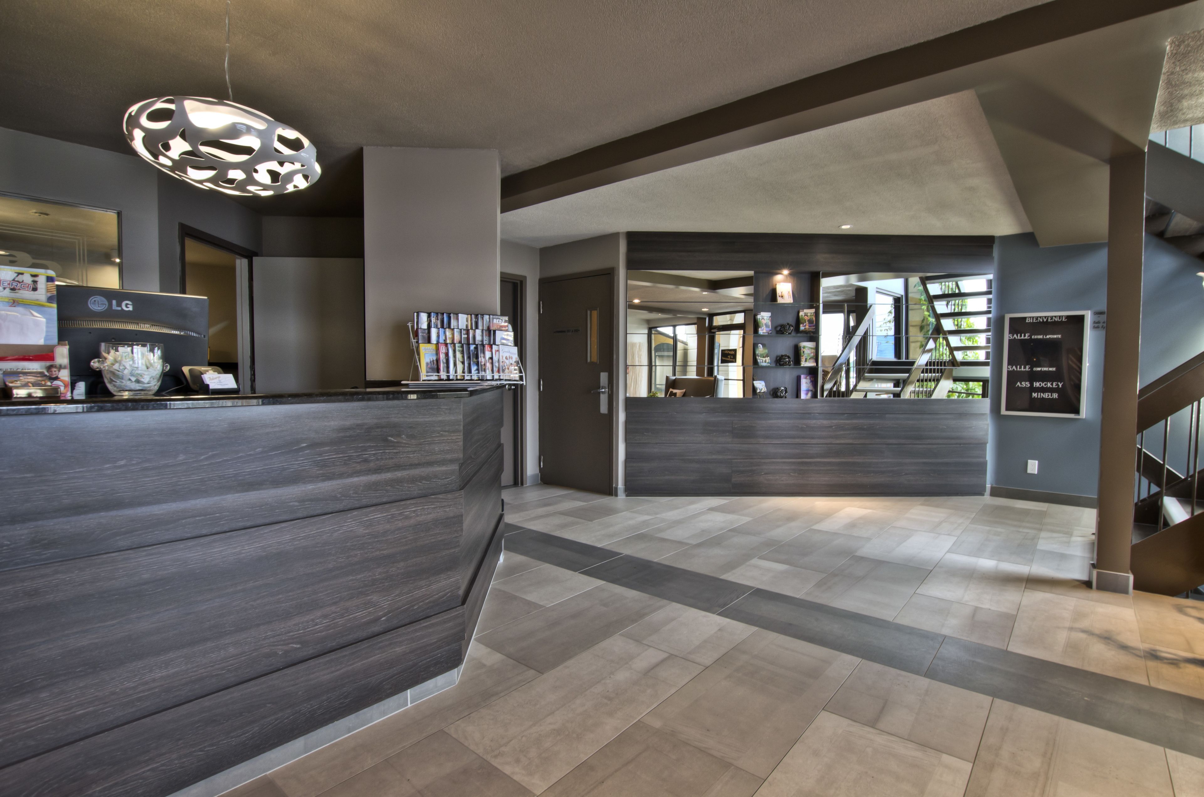 A modern reception area with a dark wood reception desk, magazines, and a sign indicating amenities like a gym and pool.