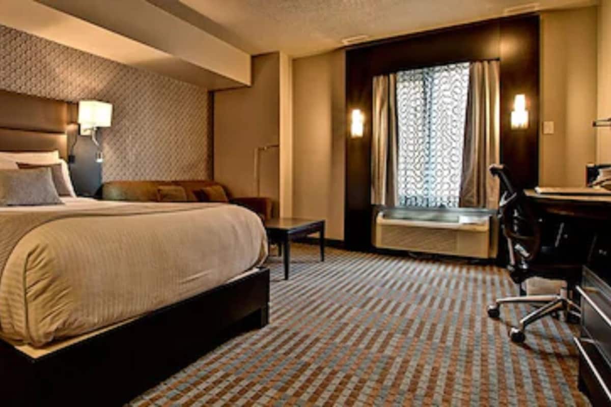 Habitación de hotel con una cama grande, un escritorio, una silla y una ventana con cortinas.