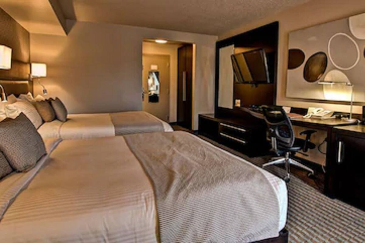 Una habitación de hotel con dos camas, un escritorio, una silla, un televisor y un espejo grande.