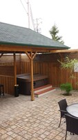 A covered patio area with a wooden deck, a barbecue grill, and a small table with chairs.