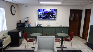 A reception area with a television, a clock, a coffee machine, a refrigerator, and two tables with chairs. - VIP Inn and Suites (Huntsville)