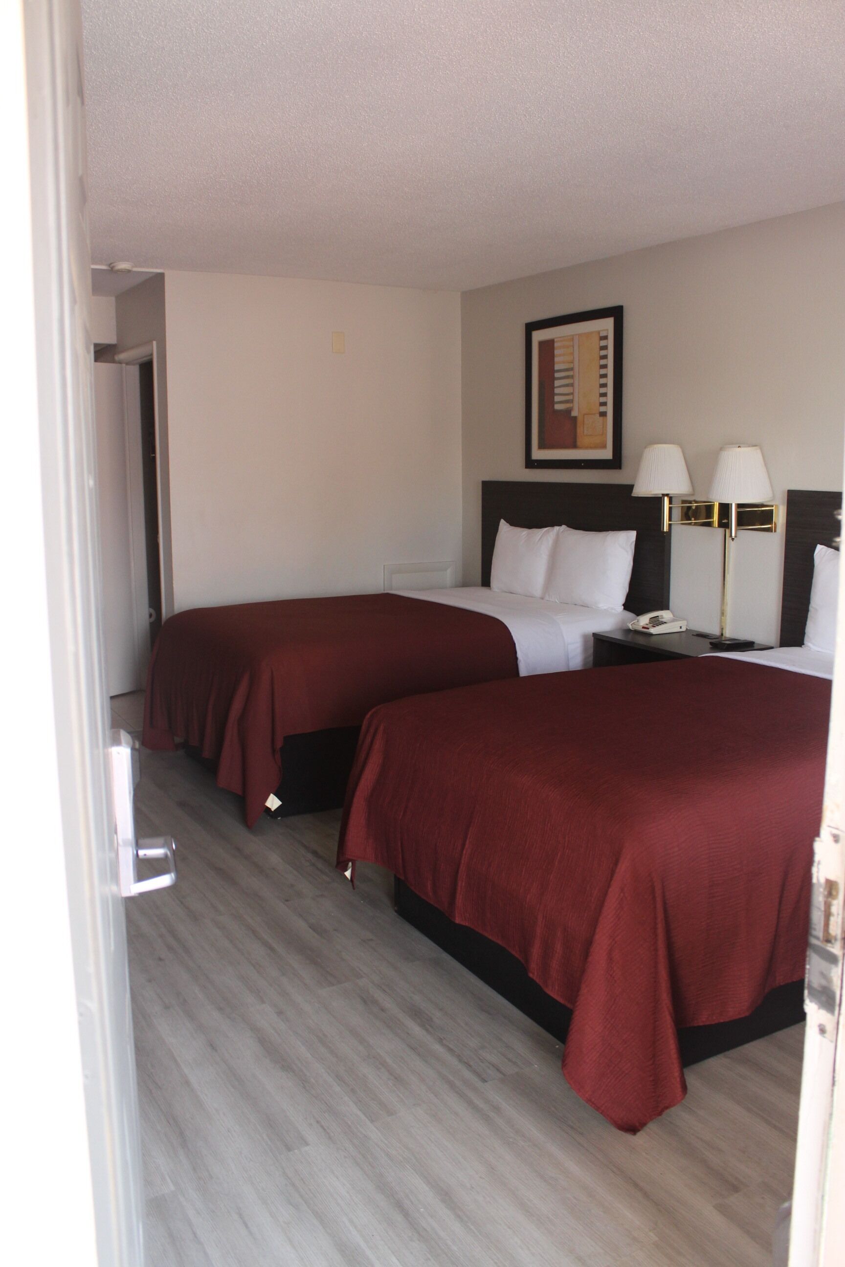 A hotel room with two beds, a nightstand, a lamp, and a painting on the wall.
