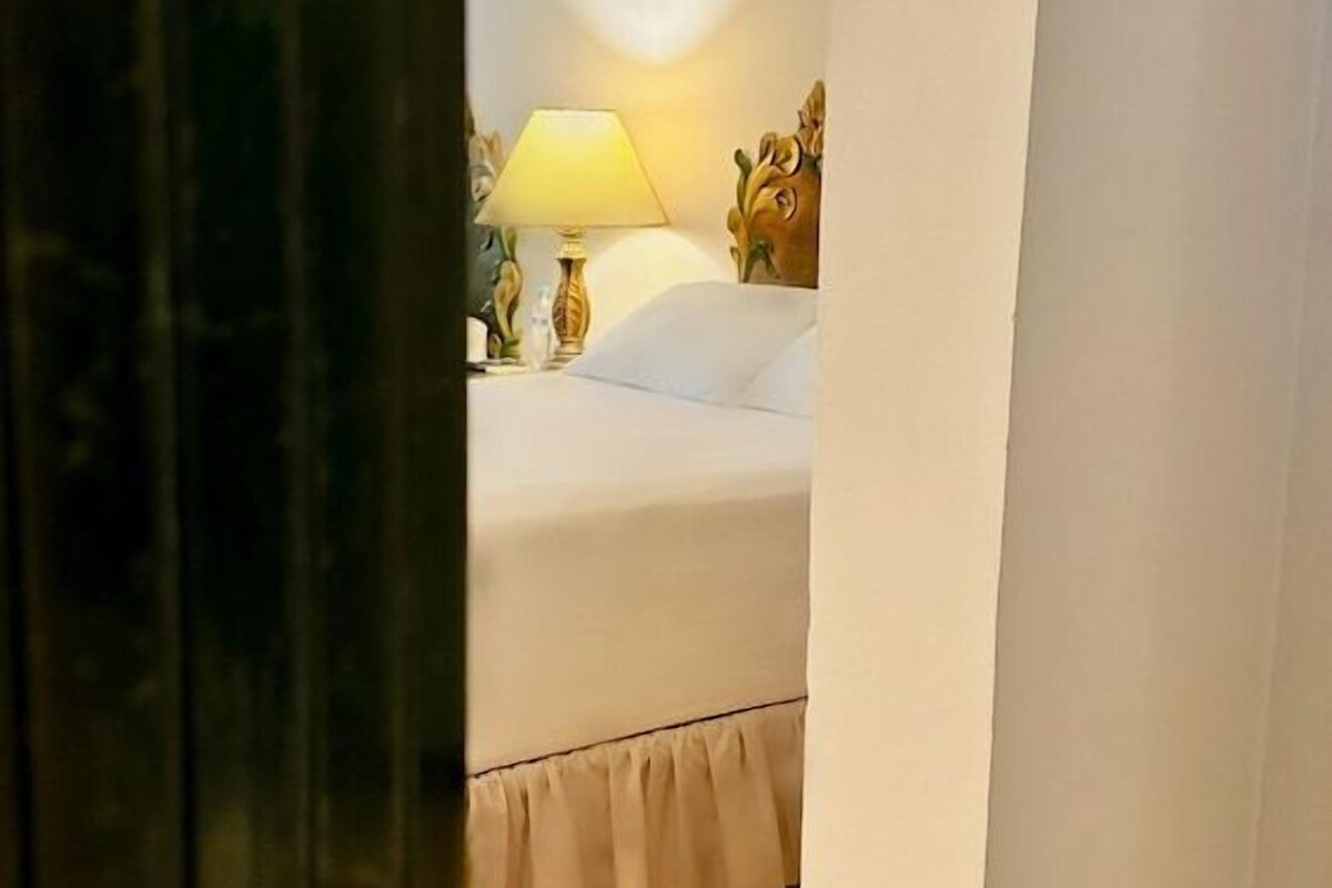 A bedroom with a bed, a nightstand, a lamp, and a curtain.