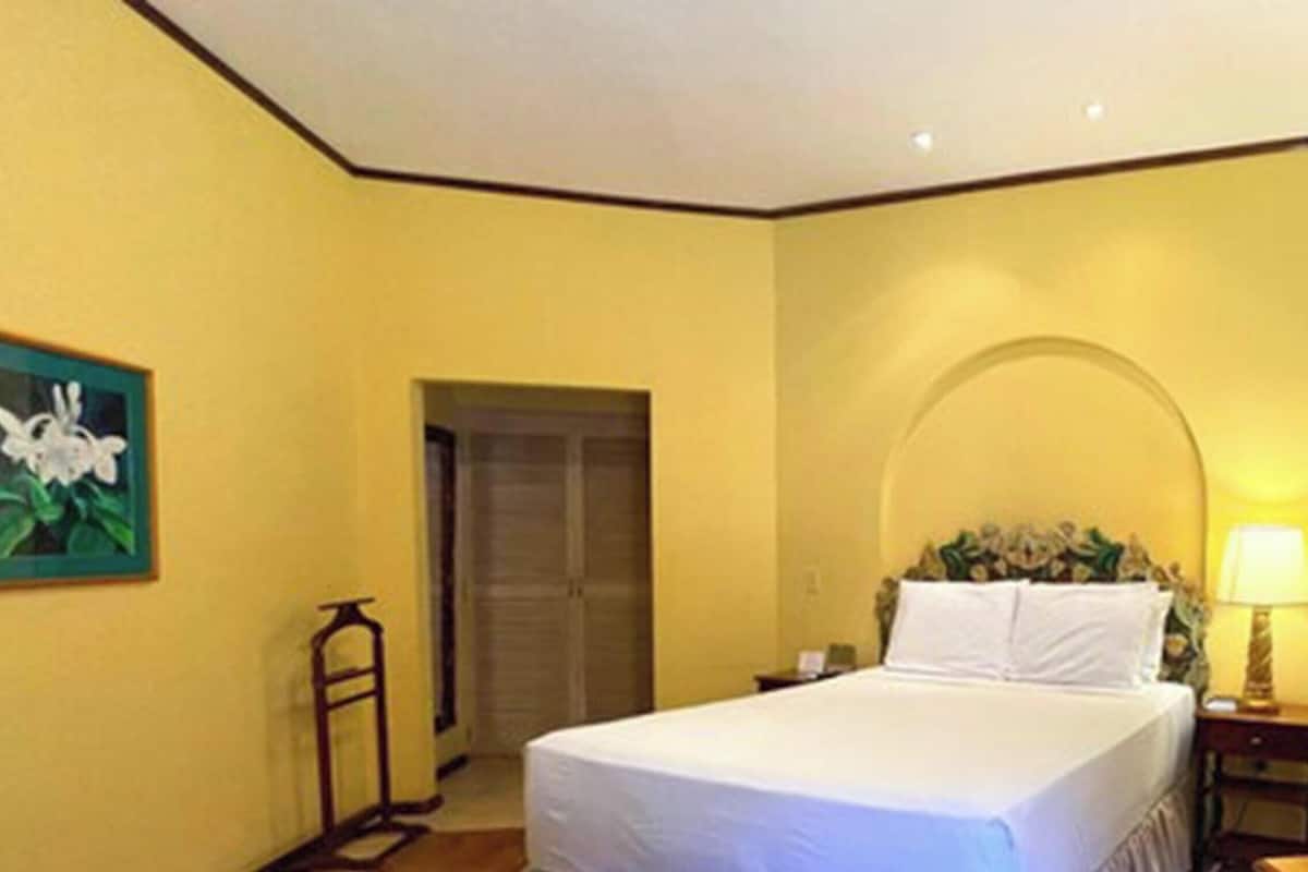 A hotel room with a bed, a nightstand, a lamp, a water bottle, and a door.