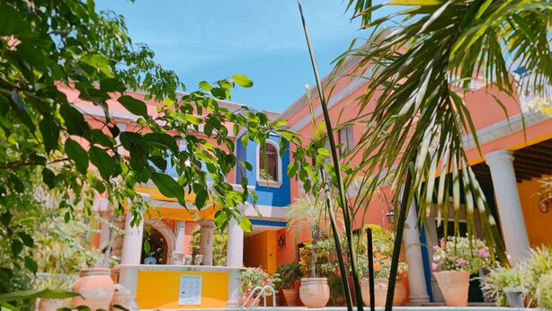 Un área de piscina con una fuente, rodeada de edificios coloridos y exuberante vegetación.