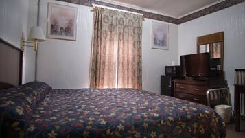 A hotel room with a large bed, a desk with a television, a lamp, and two framed pictures on the wall.