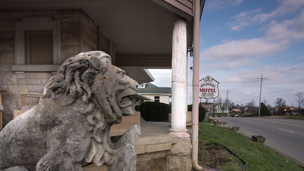 A stone lion statue in front of a motel with a green roof. - Rosemount Motel (Bedford)