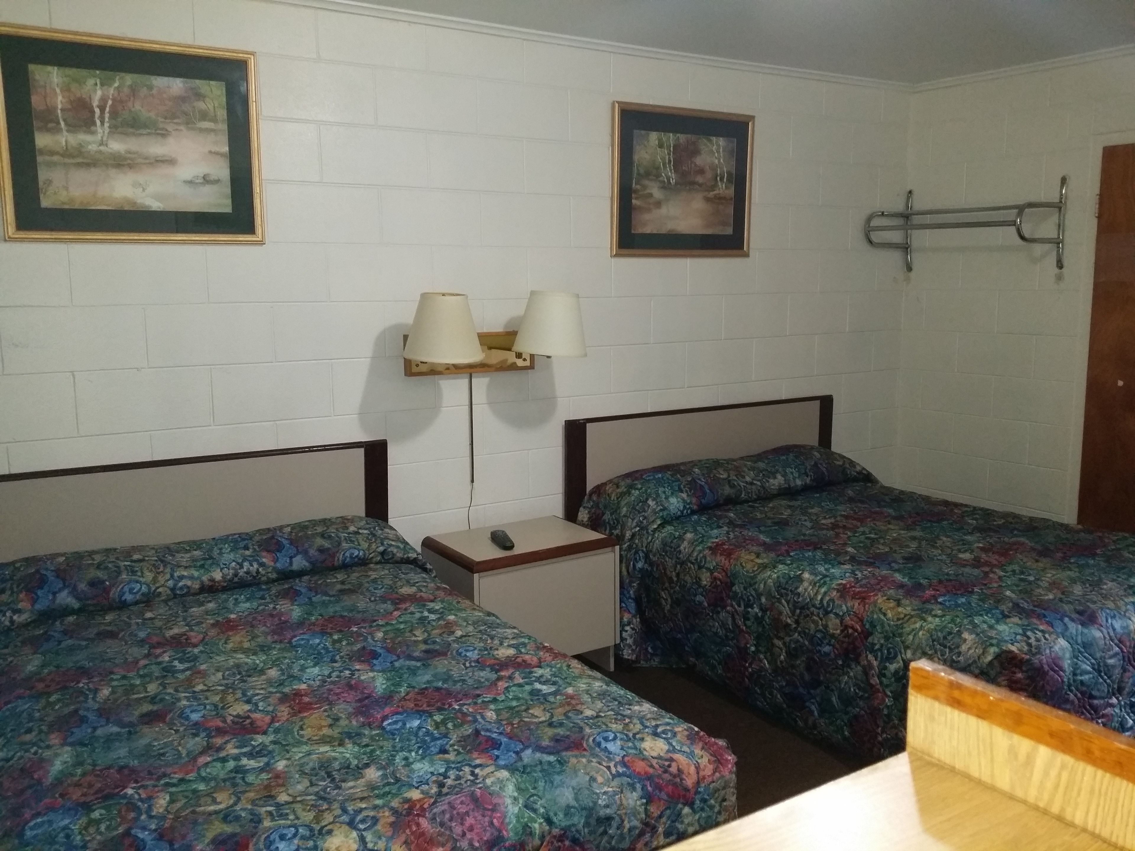 Quarto com duas camas, cada uma com colcha estampada, mesa de cabeceira com abajur e dois quadros na parede.