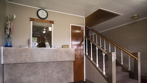 A reception desk with a clock, a 'welcome' sign, a wooden door, and a staircase. - Rosemount Motel (Bedford)