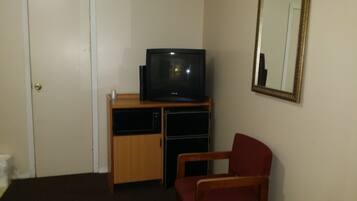 A room with a television on a wooden stand, a red chair, a bed with a floral bedspread, a door, and a mirror on the wall.
