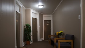 A hallway with doors numbered 101, 102, and 103, a potted plant, a small table with chairs, and a vase with flowers. - Rosemount Motel (Bedford)