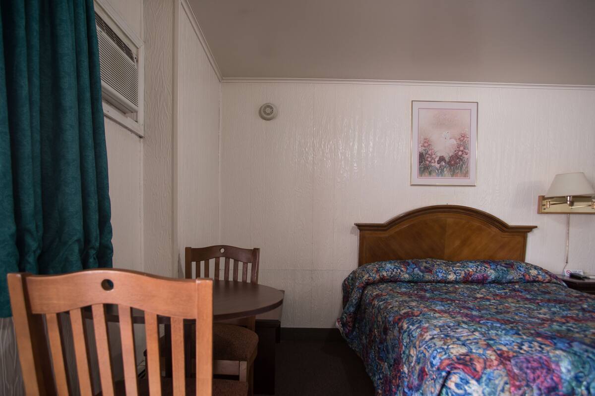 Une chambre d’hôtel avec un lit en bois, une petite table et une chaise.